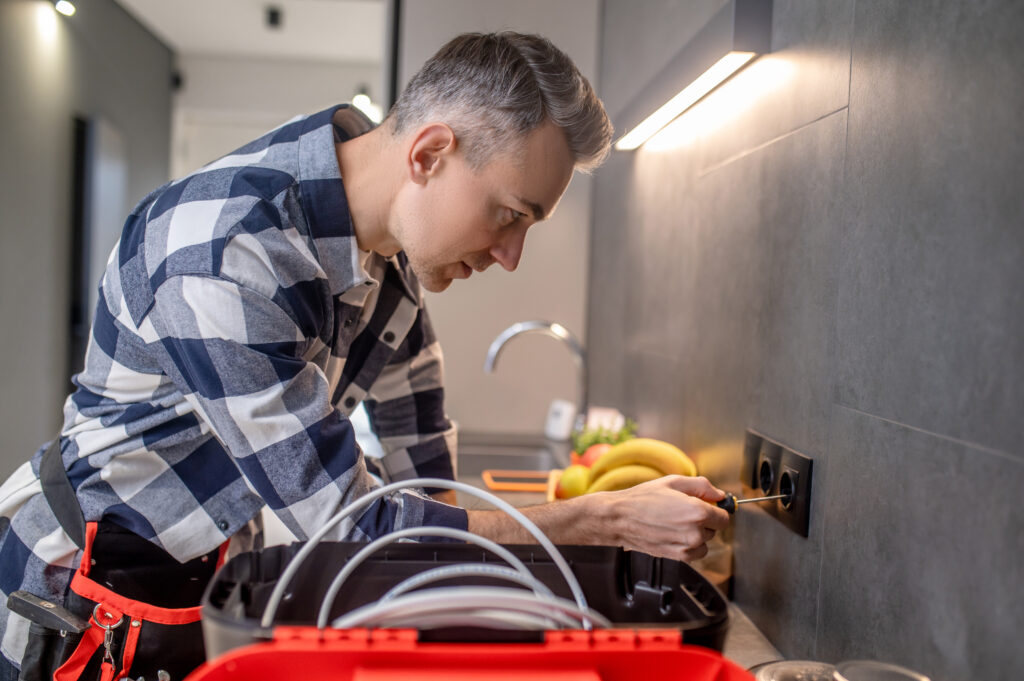 Electrician inspecting kitchen power outlet during electrical safety check